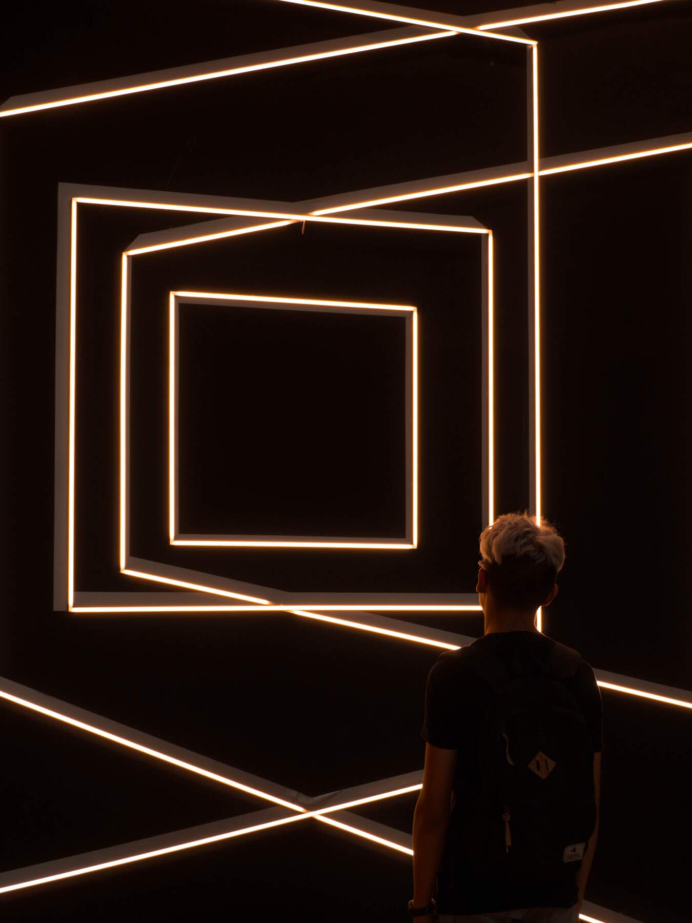 A man staring into lit and intertwined frames which signify the mixing of multiple worlds and views in the Metaverse